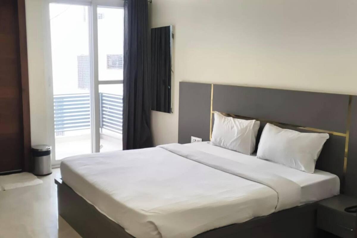 Ein Hotelzimmer mit Bett, Nachttisch, Mülleimer, Tür und einem Fenster mit Jalousien.