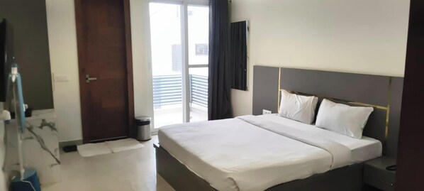 A hotel room with a bed, a bedside table, a trash bin, a door, and a window with blinds. - C T Heights Inn Bharatpur (Bharatpur)