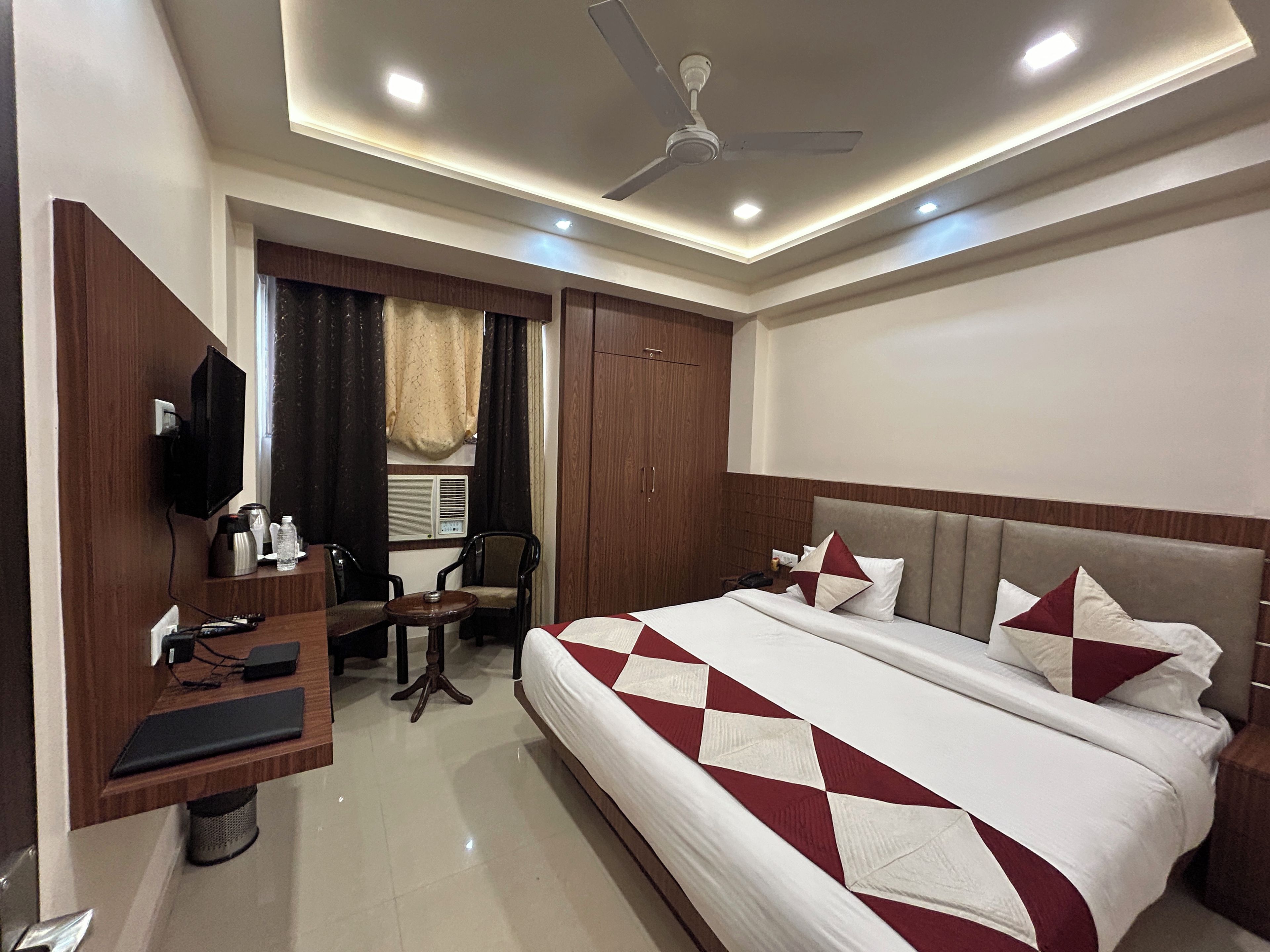 A hotel room with a bed, a desk with a chair, a television, and a ceiling fan.