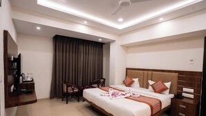 A hotel room with a bed, bedside tables, a desk with a chair, a television, and a large window with curtains. - HOTEL M K GRAND ISHWAR TOWER (Varanasi)