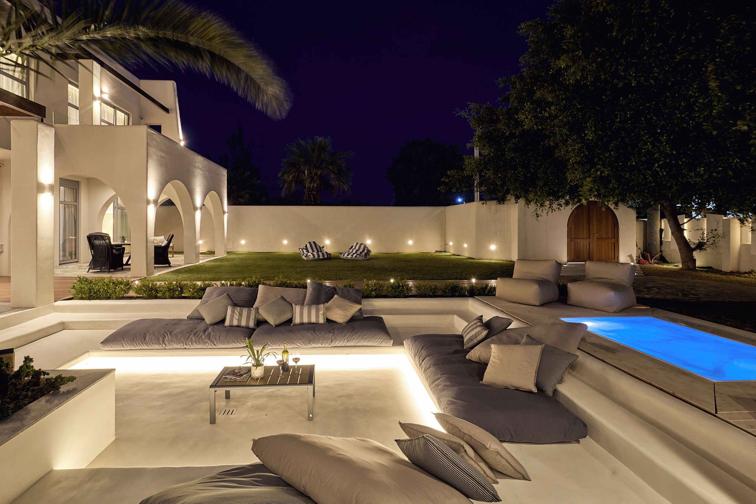 A modern outdoor living area with a pool, seating, and ambient lighting.