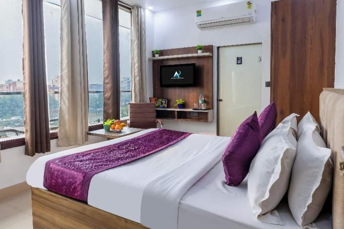 A hotel room with a bed, a TV, a ceiling fan, and a view of the city.