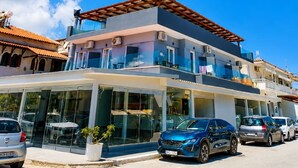 A modern multi-story building with a glass facade, a flat roof, and a parking area with several cars. - New Horizon Sarti - Double Room with Balcony G2 (Sarti)