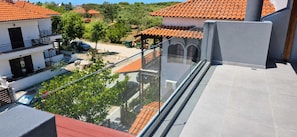 Ein Wohngebäude mit Balkon, der auf einen Innenhof mit Bäumen und einem parkenden Auto blickt.