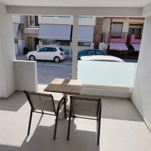 Ein Balkon mit Tisch und Stühlen mit Blick auf eine Straße, gesäumt von parkenden Autos und Gebäuden.