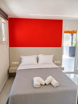 Ein modernes Hotelzimmer mit einem großen Bett, einer roten Akzentwand und Blick ins Freie.