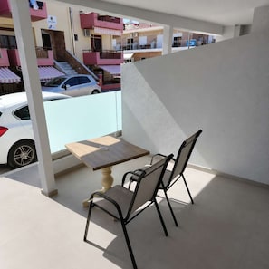 Ein Balkon mit Tisch und zwei Stühlen mit Blick auf eine Straße, gesäumt von parkenden Autos und Gebäuden.