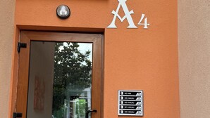 Een gevelingang met een glazen deur, een metalen hekwerk en een wandbord waarop de verdiepingen en kamersaantallen staan.