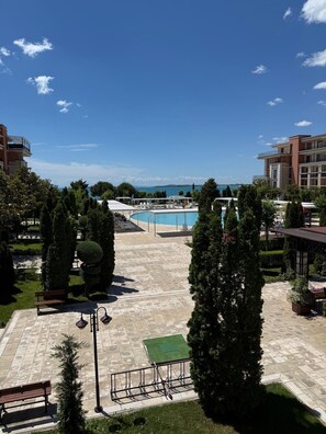 A pool area with a view of the sea, surrounded by greenery and buildings. - Cozy Beachfront Apt with Pool @ Prestige Fort Beach⁠ (Sveti Vlas)