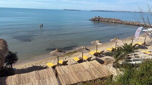 Een strand met helder water, een rotsenwerende steiger en gele strandstoelen.