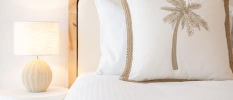 A bed with a wooden headboard, white bedding, and a palm tree embroidered pillow.