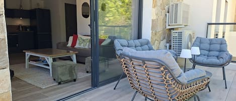 Un espacio moderno para estar con puerta de vidrio corredera que da a un balcón, una mesa de comedor y dos sillones acolchados.