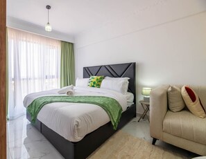 Ein modernes Schlafzimmer mit Bett, Nachttisch, Lampe und einer Couch.