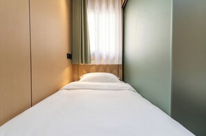 Una cama individual con ropa de cama blanca en una habitación de hotel.
