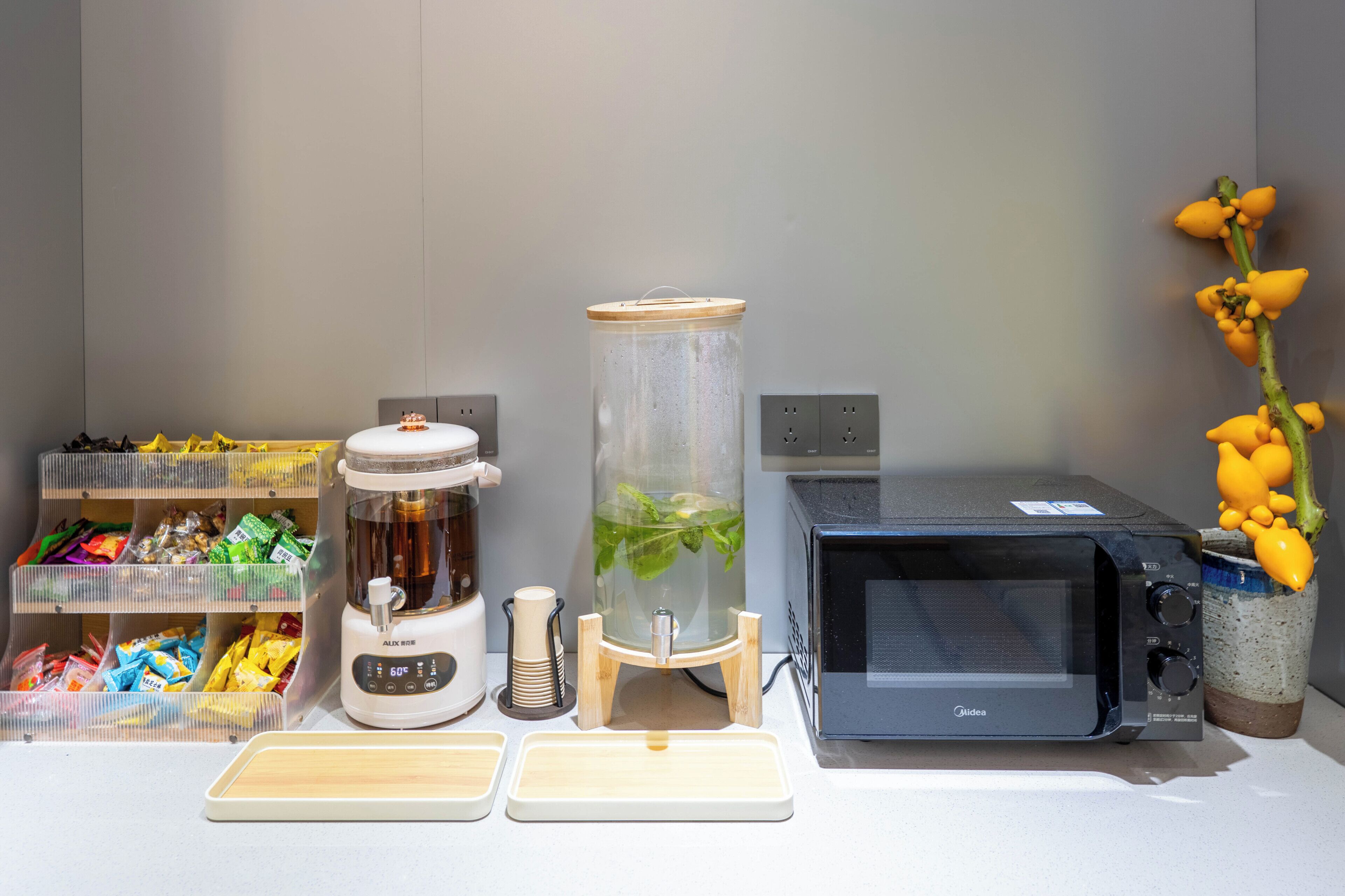 A kitchen counter with a coffee maker, a glass container with a plant, a microwave, and a shelf with snacks.