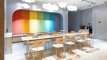 Un interior moderno con una mesa larga y sillas, una pared colorida y un techo con luces con forma de nubes.