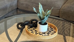 A living room with a grey sofa, a blue pillow, a white vase with a plant, and a woven tray.