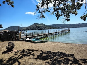 Un muelle a orillas del lago con barcos, un embarcadero de madera y una colina distante.