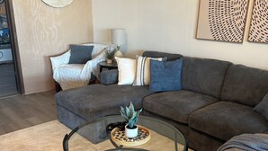 A modern living room with a sectional sofa, a glass coffee table with a plant, and decorative wall art.