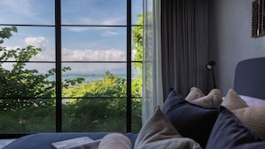 Ein Schlafzimmer mit großem Fenster, einem Bett mit Kissen und einer Nachttischlampe.