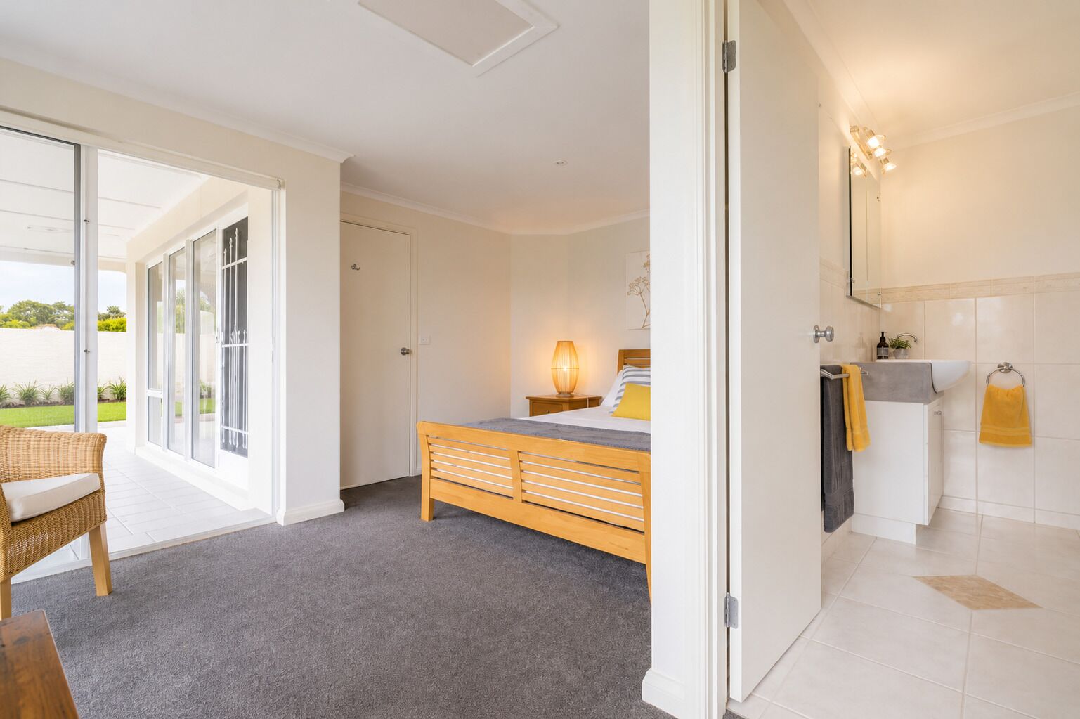 Une chambre à coucher comprenant un lit, une table de chevet, une lampe et une vue sur un balcon, accessible par une porte coulissante.