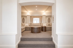Ein modernes Wohnzimmer mit einer Eckcouch, zwei Beistelltischen und einer Treppe, die zu einer oberen Etage führt.