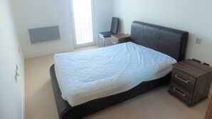 A bedroom with a bed, a chair, a bedside table, and a small wooden cabinet. - Spacious 2 Bedroom Apartment in the Heart of the City (Cardiff)