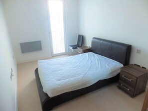 A bedroom with a bed, a chair, a bedside table, and a small wooden cabinet. - Spacious 2 Bedroom Apartment in the Heart of the City (Cardiff)