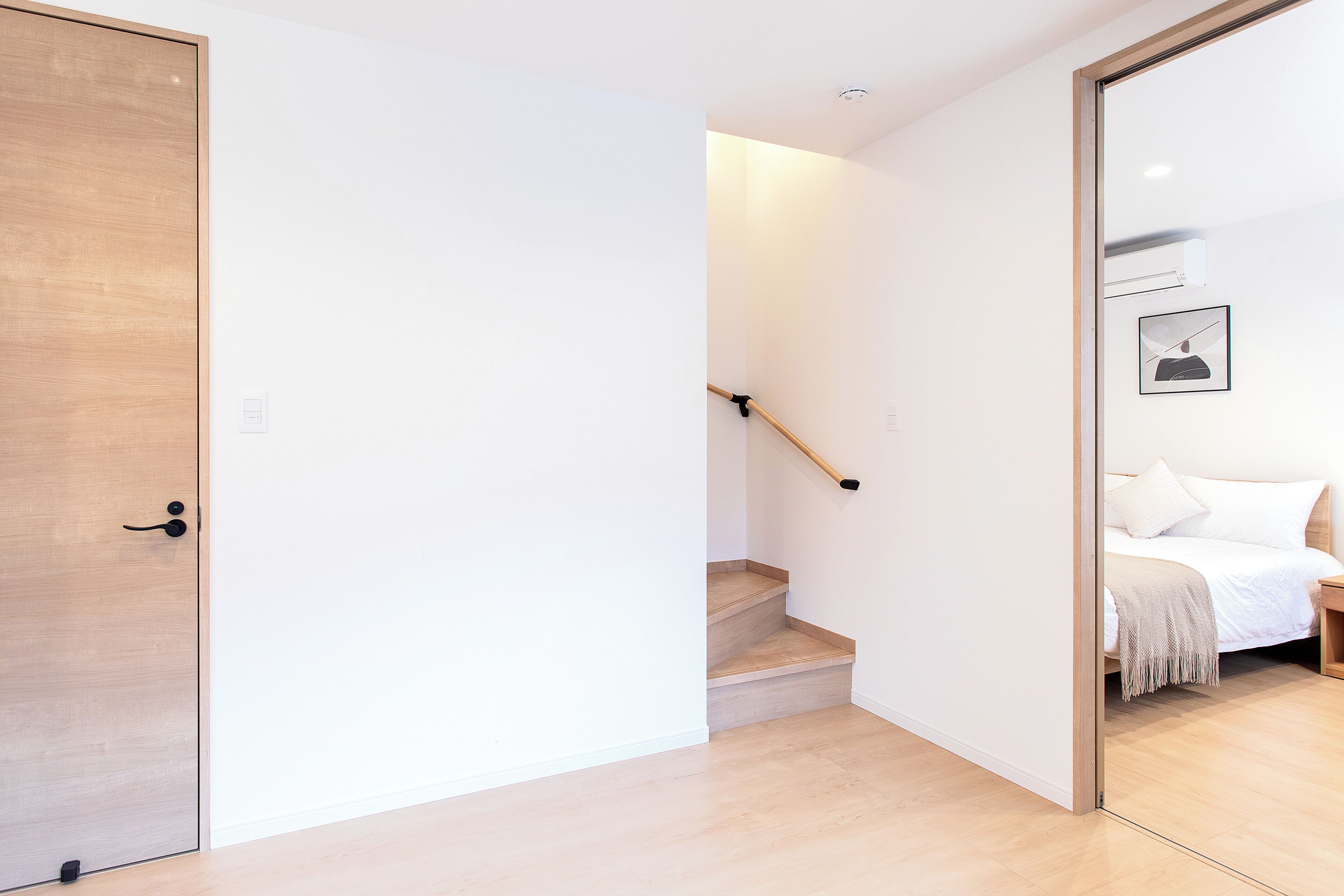A modern interior with a wooden door, a staircase, and a bed with a white headboard.