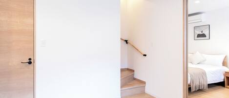 A modern interior with a wooden door, a staircase, and a bed with a white headboard.
