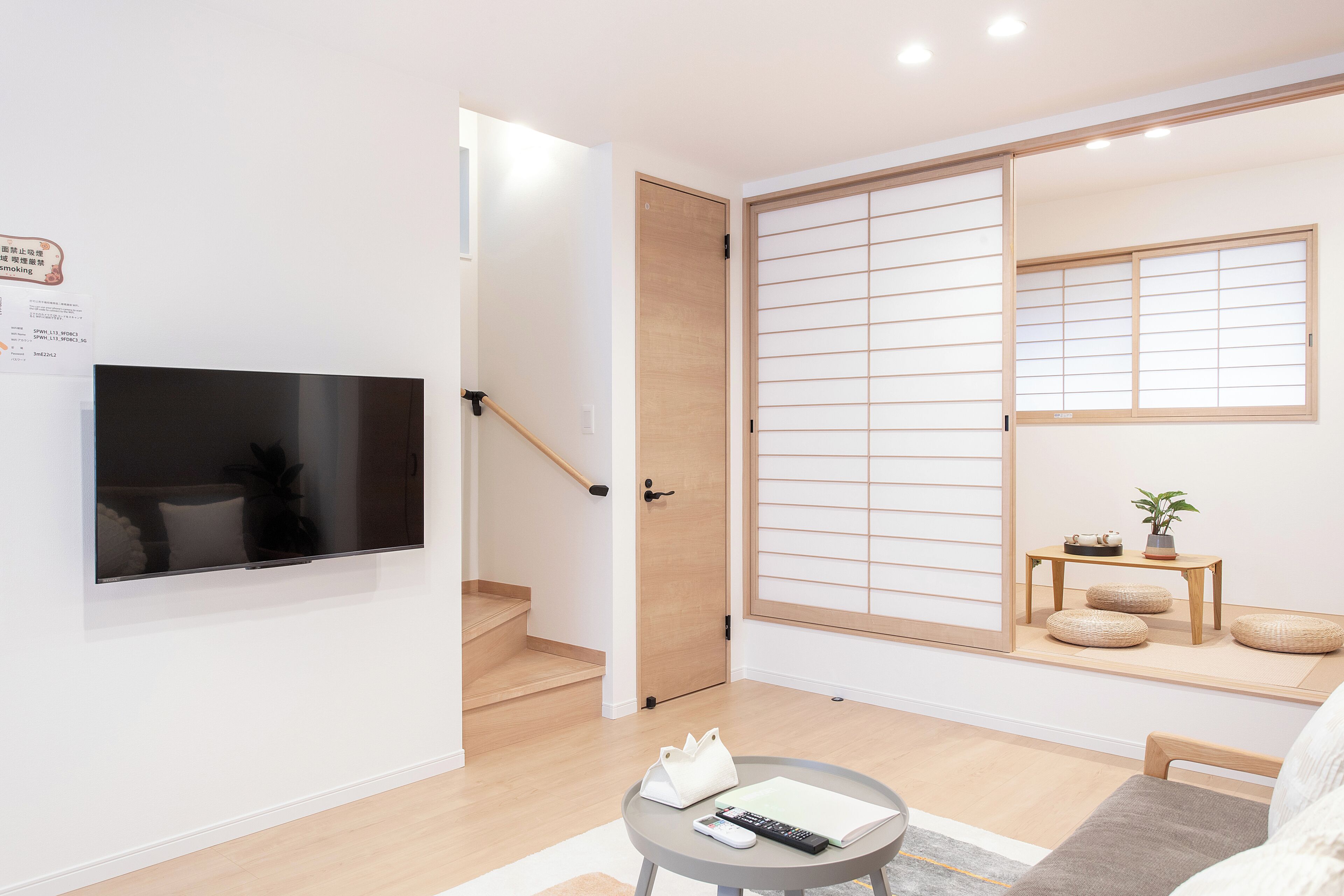 A modern living room with a flat-screen TV, a wooden door, a sliding shoji screen, a small wooden table with a plant, and a sofa.