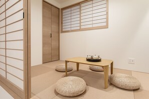 A room with tatami flooring, a sliding door, a small table with a tea set, and woven floor cushions. - SHOTENSHITA (Osaka)