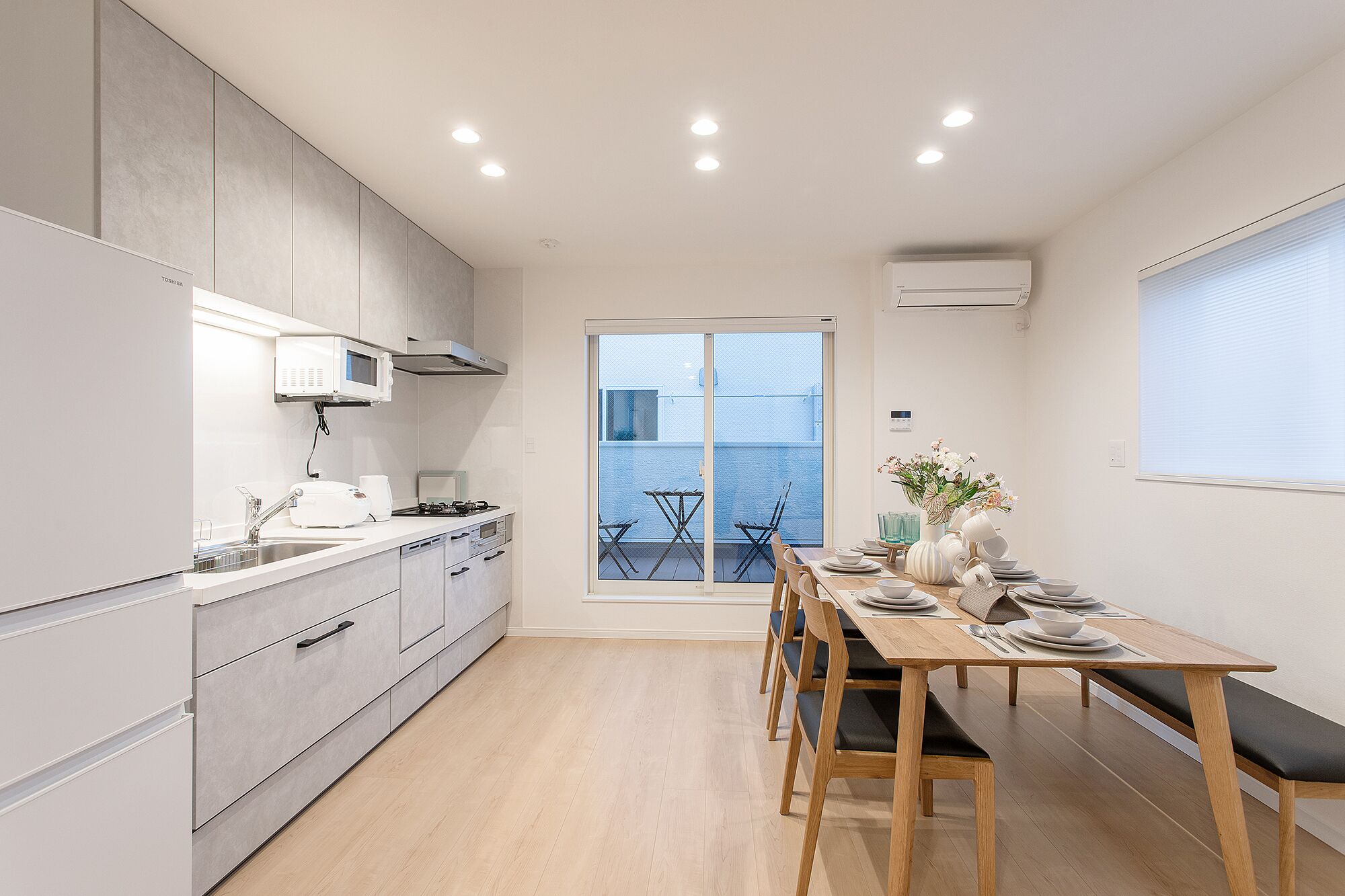 A modern kitchen with a dining area, a sliding glass door to the outside, and a white air conditioning unit on the wall.