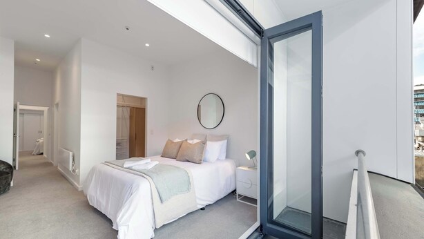 A modern bedroom with a bed, bedside table, and a large window.