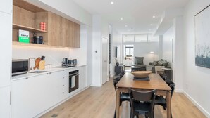A modern kitchen with white cabinets, a wooden dining table, and a large window.