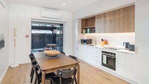 A modern kitchen with white cabinets, a wooden dining table, and a built-in oven.