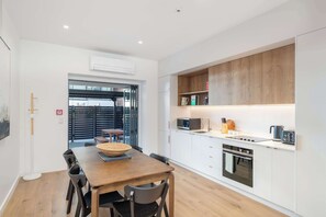 A modern kitchen with white cabinets, a wooden dining table, and a built-in oven.