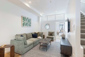 A modern living room with a sectional sofa, a coffee table, a small side table, and a TV mounted on the wall. - The Ascot | 3BR + Patio | Courtenay Place (Wellington)