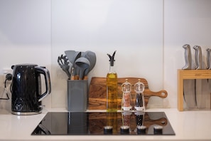 Eine Küchenarbeitsplatte mit einem schwarzen Wasserkocher, einer Flasche Olivenöl, Salz- und Pfeffermühlen, einem Holzschnittbrett und einem Messerblock.