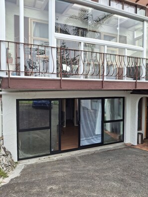 Ein zweistöckiges Gebäude mit großen Fenstern, einem Balkon mit Metallgeländer und einer Tür, die zu einem Innenbereich führt.