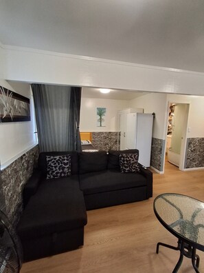 Ein Wohnzimmer mit Ecksofa, Glastisch und einer Küche im Hintergrund.