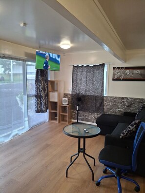 Ein Wohnzimmer mit Fernseher, Ventilator, Tisch, Sofa und einem Fenster mit Vorhängen.
