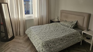 Ein Schlafzimmer mit einem Bett, einem Nachttisch, einem Spiegel und einem Fenster mit Vorhängen.