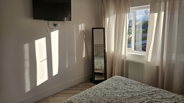 Ein Schlafzimmer mit einem Bett, einem an der Wand befestigten Fernseher, einem Fenster mit Vorhängen und einer Heizung.