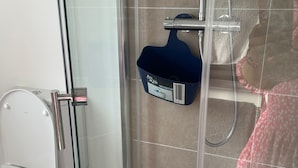 Ein Duschkabine mit Glaswänden, eine Handbrause, eine blaue Seifenschale und eine Toilette links davon.