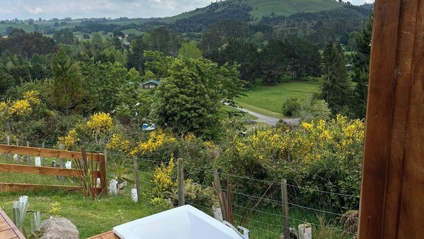 Eine Holzterrasse mit einer weißen Badewanne, umgeben von viel Grün und Blick auf sanfte Hügel.