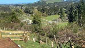 Ländliche Landschaft mit einer Holzterrasse, einem eingezäunten Bereich und Blick auf einen Hügel mit vereinzelten Bäumen.