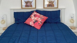 Ein Schlafzimmer mit einer Tonnenwölbung, einem Bett mit blauer Bettwäsche, einem roten Kissen mit Blumenmuster und zwei gerahmten Bildern an der Wand.