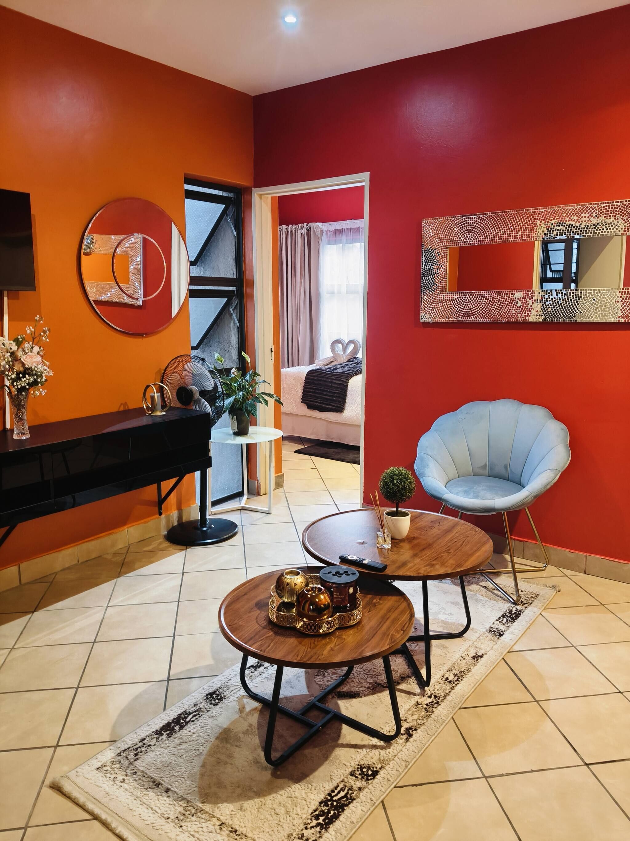 A modern living room with a red accent wall, a round coffee table, a blue chair, and a sofa with a heart-shaped decoration.