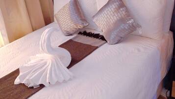 A neatly made bed with white linens and decorative pillows, a wooden headboard, and a dark-colored rug.
